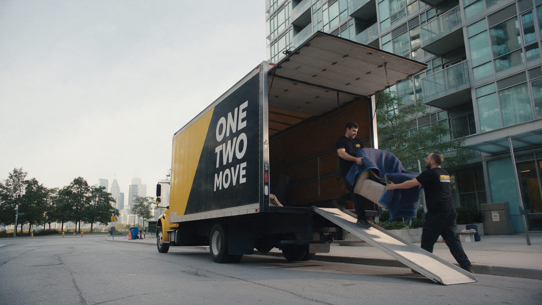 One Two Move crew loading a wrapped armchair into a branded truck outside a Toronto condo tower